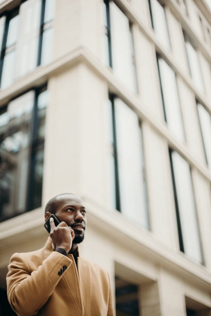 Homme confiant en trench-coat téléphonant à l'extérieur devant un bâtiment moderne.