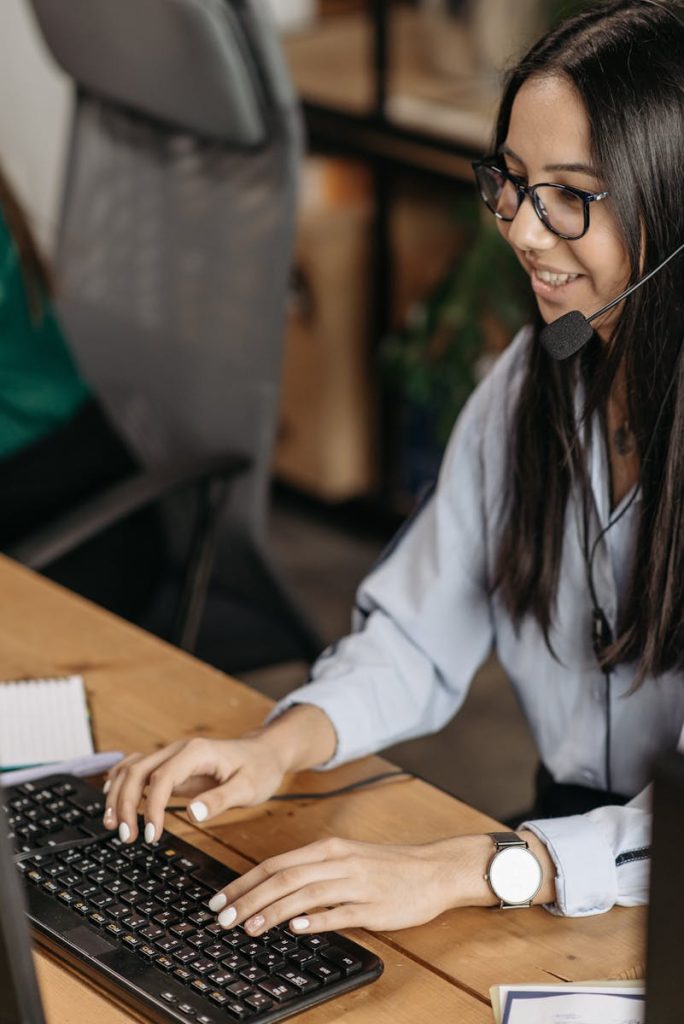 Femme joyeuse dans un centre d'appel, tapant sur un clavier, portant un casque et des lunettes.