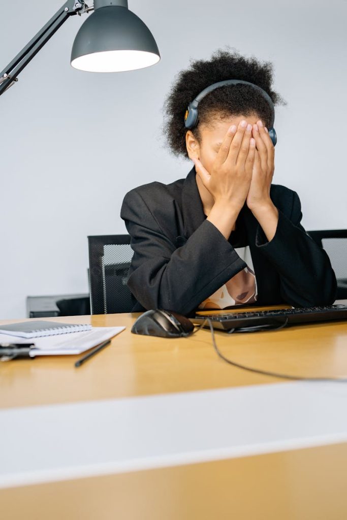 Une employée fatiguée d'un centre d'appel se couvrant le visage avec les mains en signe de frustration, portant un casque dans un bureau.